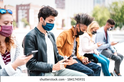 Multiracial friends using mobile phones covered by face mask on Covid second wave - Worried guys and girls watching news on smartphone devices - College students sitting at university campus break