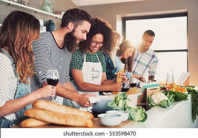 Multiracial funny friends cook some tasteful food at kitchen while drinking wine. - Shutterstock ID 553598470