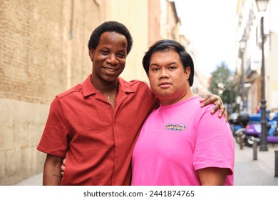 Multiracial gay couple smiling at street, one wearing a red shirt and the other wearing a pink shirt. - Powered by Shutterstock