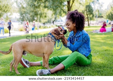 Multiracial girl sitting and resting with her dog outside in the park, training him, spending leisure time together. Concept of relationship between dog and teenager, everyday life with pet.