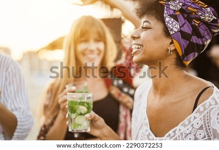 Multiracial girls having fun dancing and drinking with cocktails at bar on the beach - Focus on african girl ear