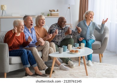 Multiracial gorup of emotional senior people watching football game on TV and drinking tea with cupcakes in the living room, spending good time together at cozy nursing home, gesturing and screaming - Powered by Shutterstock