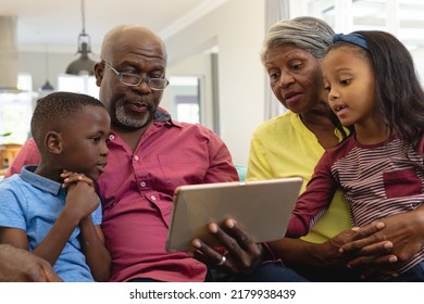 Multiracial Grandparents With Grandchildren Watching Video Over Digital Tablet While Sitting At Home. Wireless Technology, Unaltered, Family, Togetherness, Childhood And Retirement Concept.