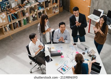Multiracial group of Asia young creative people in smart casual wear discussing business clapping, laughing and smiling together in brainstorm meeting at office. Coworker teamwork successful concept.
