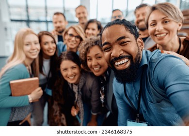 Multiracial group of cheerful business seminar attendees taking selfie in conference hall and looking at camera.  - Powered by Shutterstock