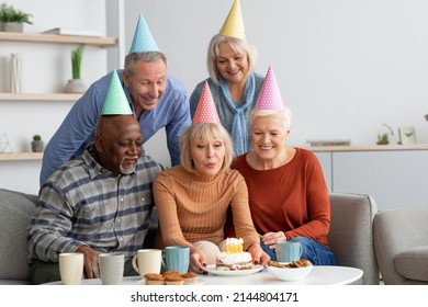 Multiracial group of elderly people happy men and women wearing colorful paper hats having birthday party at home, caucasian senior lady blowing off candles on birthday cake, copy space - Powered by Shutterstock