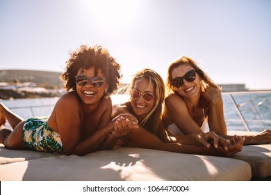 Multiracial group of females wearing sunglasses lying on the bow of a yacht on a summer day. Three young women sunbathing on private yacht.