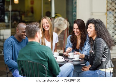 Multiracial group of five friends having a coffee together. Three women and two men at cafe, talking, laughing and enjoying their time. Lifestyle and friendship concepts with real people models