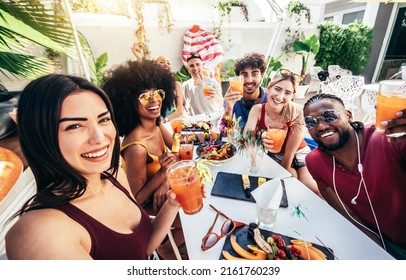 Multiracial Group Of Friends Enjoying Meal Having Backyard Dinner Party - Young People Toasting Cocktail Glasses Together At Bar Restaurant - Social Gathering Concept With Guys And Girls Taking Selfie