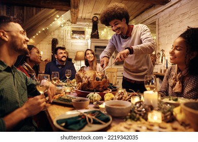 Multiracial group of friends gathering at dining table for Thanksgiving dinner. Focus is on man carving roast turkey. - Powered by Shutterstock