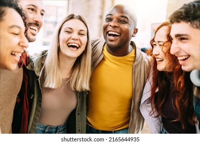 Multiracial group of friends having fun together on city street - Millenial people laughing hugging outside - Friendship concept with guys and girls enjoying hanging outside 