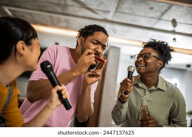 Multiracial group of friends having karaoke night. Singing in to the microphone, drinking beer and playing mouth organ. - Powered by Shutterstock