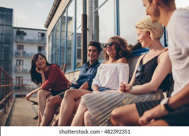 Multiracial group of friends sitting in balcony and smiling. Young people relaxing outdoors in terrace. - Powered by Shutterstock