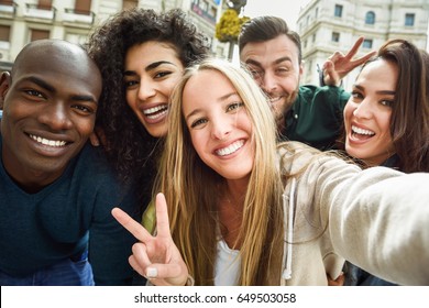 Multiracial group of friends taking selfie in a urban street with a blonde woman in foreground. Three young women and two men wearing casual clothes. - Powered by Shutterstock