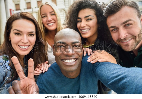 都市の街並みで自撮りをする多民族の友人のグループで 前景に黒人の男性がいる 3人の若い女性と2人の男性が普段着です の写真素材 今すぐ編集