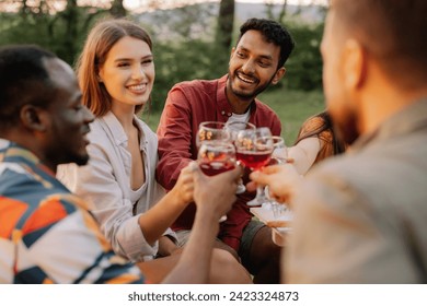 Multiracial group of happy friends sitting around table drinking wine talking at dinner party in evening summer forest - Powered by Shutterstock