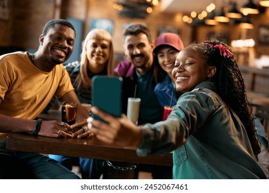 Multiracial group of happy friends taking selfie in a pub. Focus is on African American woman taking picture. - Powered by Shutterstock