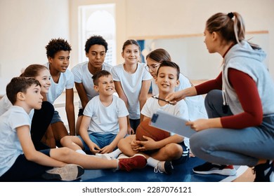 Multiracial group of happy students talking to their sports teacher during basketball class at school. - Powered by Shutterstock