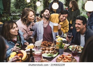 Multiracial group of hilarious friends have fun drinking beer and wine and eating together on the weekend at the restaurant table in the countryside - focus on bearded man in the center - Powered by Shutterstock