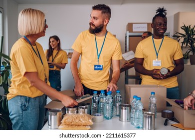 Multiracial Group Of People Working On Humanitarian Aid Project. Teamwork In Homeless Shelter. Small Diverse Group Of Volunteers Working In A Community Charity Donation Center. Focus On A Bearded Man