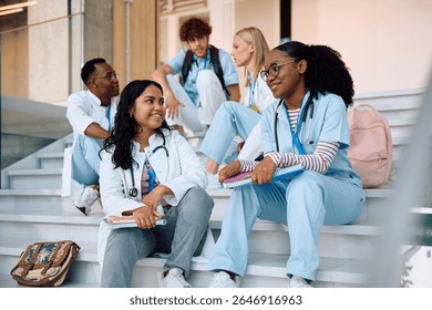 Multiracial group of students communicating while sitting on staircase at medical university.