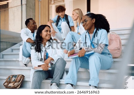 Multiracial group of students communicating while sitting on staircase at medical university.