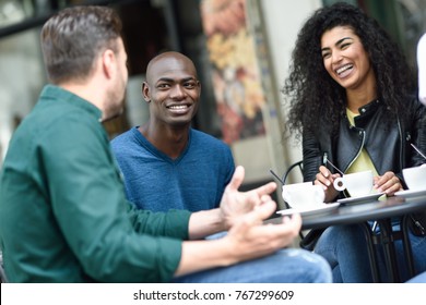 Multiracial group of three friends having a coffee together. A woman and two men at cafe, talking, laughing and enjoying their time. Lifestyle and friendship concepts with real people models
