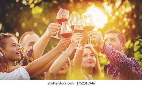 Multiracial group of young friends toasting wine glasses at outdoor party - Friendship celebration with happy people enjoying time together at vineyard restaurant garden drinking red wine at sunset