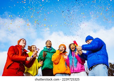 Multiracial group of young happy friends meeting outdoors in winter and celebrating party with confetti shooter, wearing winter jackets and having fun - Multiethnic millennials bonding in a urban area