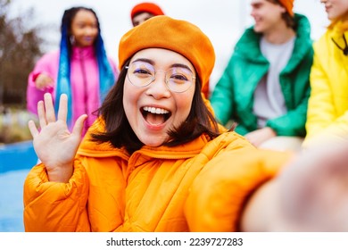 Multiracial group of young happy friends meeting outdoors in winter, wearing winter jackets and having fun, asian woman taking pov selfie - Multiethnic millennials bonding in a urban area - Powered by Shutterstock