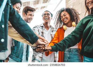 Multiracial group of young people stacking hands outdoors - Happy friends celebrating success on city street - Youth community concept with guys and girls standing together supporting peace and love - Powered by Shutterstock