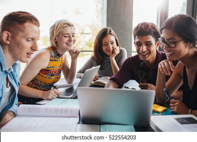 Multiracial Group Of Young Students Studying In The Library. Young People Sitting Together At Table With Books And Laptop For Researching Information For Their Project.