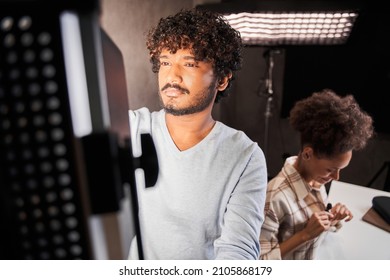Multiracial guy standing in front of the lighting equipment and correcting