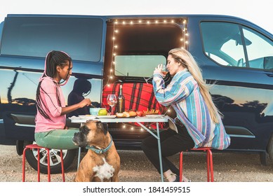 Multiracial happy friends celebrating in front of camper van while eating organic food with their dog - Focus on faces