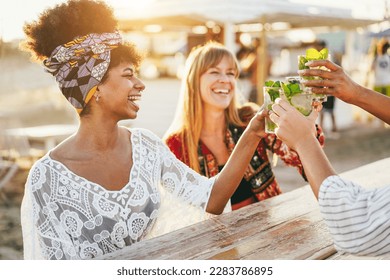 Multiracial happy friends cheering and drinking mojitos at beach party - Focus on right hand holding cocktail