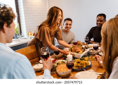 Multiracial happy friends eating turkey during thanksgiving dinner at home - Powered by Shutterstock