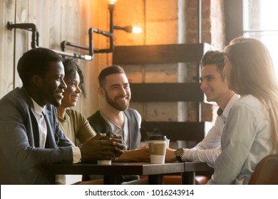 Multiracial Happy Friends Talking And Drinking Coffee Sharing Coffeehouse Table, Diverse African And Caucasian Millennial Young People Smiling Enjoying Pleasant Conversation In Cafe At Coffee Break