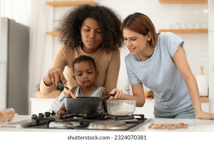 Multiracial lesbian couple cooking healthy food in kitchen for their biracial child. Beautiful gay women standing at counter enjoy preparing lunch at home with kid. Happy LGBT family eating lifestyle. - Powered by Shutterstock