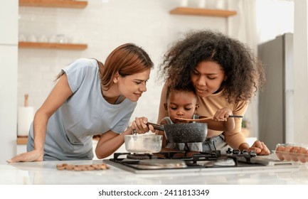 Multiracial lesbian couple cooking healthy food in kitchen for their biracial boy. Gay women standing at counter enjoy preparing lunch at home with child kid. Young adult LGBT family eating together - Powered by Shutterstock