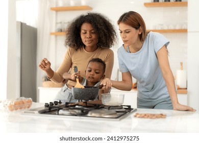 Multiracial lesbian couple cooking healthy food in kitchen for their biracial boy. Gay women standing at counter enjoy preparing lunch at home with child kid. Young adult LGBT family eating together - Powered by Shutterstock