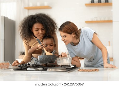 Multiracial lesbian couple cooking healthy food in kitchen for their biracial boy. Gay women standing at counter enjoy preparing lunch at home with child kid. Young adult LGBT family eating together - Powered by Shutterstock