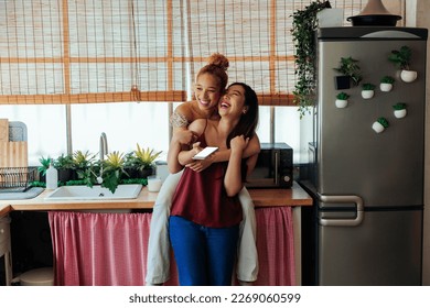 A multiracial lesbian couple hugging and laughing while surfing the internet on a phone - Powered by Shutterstock