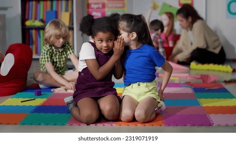 Multiracial little girls tell secrets sitting on floor in kindergarten. Adorable preschool African-American and caucasian girls sitting together in playroom share secrets - Powered by Shutterstock