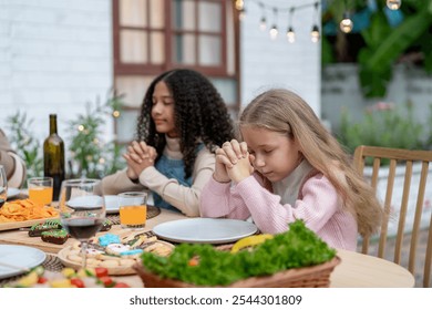 Multiracial lovely children say a prayer before having dinner party. Adorable young girls closing eyes and making a wish, celebrating holiday Thanksgiving Chrsitmas on dining table outdoors at home. - Powered by Shutterstock