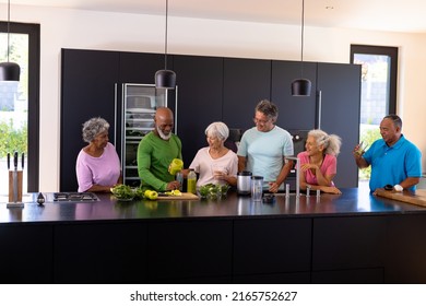 Multiracial male and female seniors talking and preparing vegetables and fruits smoothie in kitchen. Retirement home, unaltered, friendship, togetherness, support, assisted living, healthy food. - Powered by Shutterstock