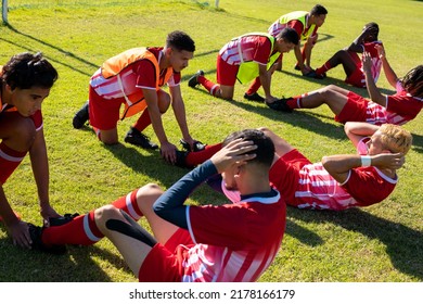 Multiracial male players holding legs of teammates practicing crunches on grassy field at playground. Assisting, unaltered, soccer, sport, teamwork, competition, exercising, training and fitness. - Powered by Shutterstock