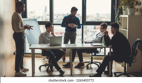 Multiracial male staff of architectural and design bureau communicating in modern loft office with panoramic view, discussing individual orders of the clients on design and planning of interiors. - Shutterstock ID 1265403772