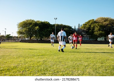 Multiracial Male Teams Playing Soccer Match In Playground Against Clear Sky On Sunny Day, Copy Space. Rivalry, Summer, Unaltered, Soccer, Sport, Teamwork, Togetherness And Competition Concept.