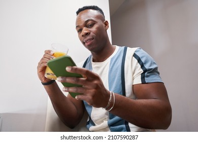 Multiracial man staring at smartphone while drinking juice