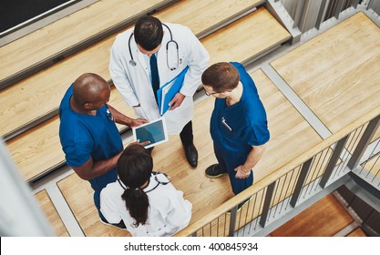 Multiracial medical team having a discussion as they stand grouped together around a tablet computer on a stair well, overhead view